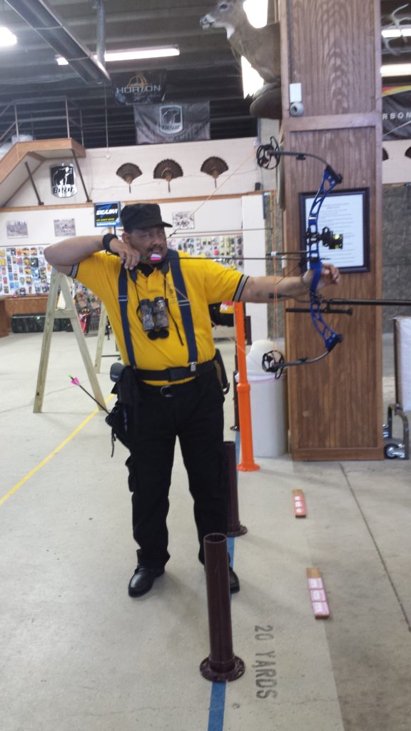 A man in yellow shirt holding a bow and arrow.