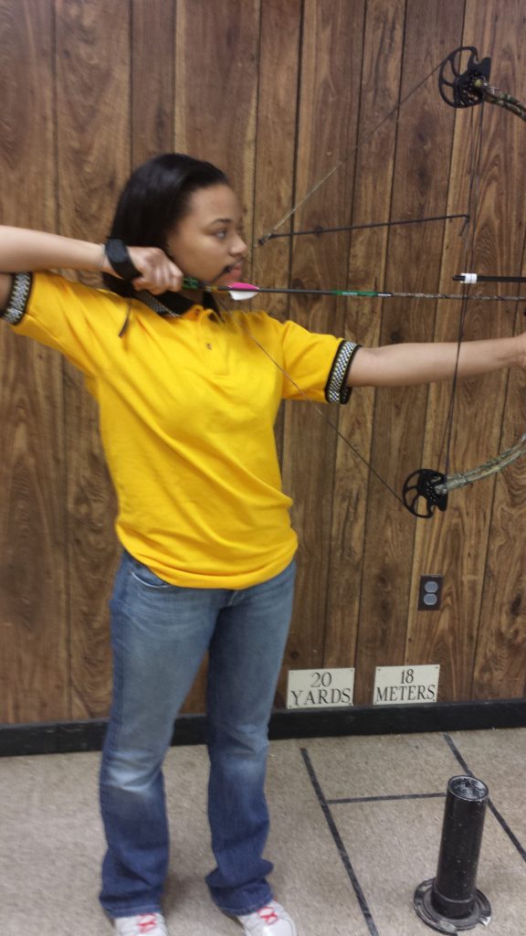 A woman in yellow shirt holding a bow and arrow.